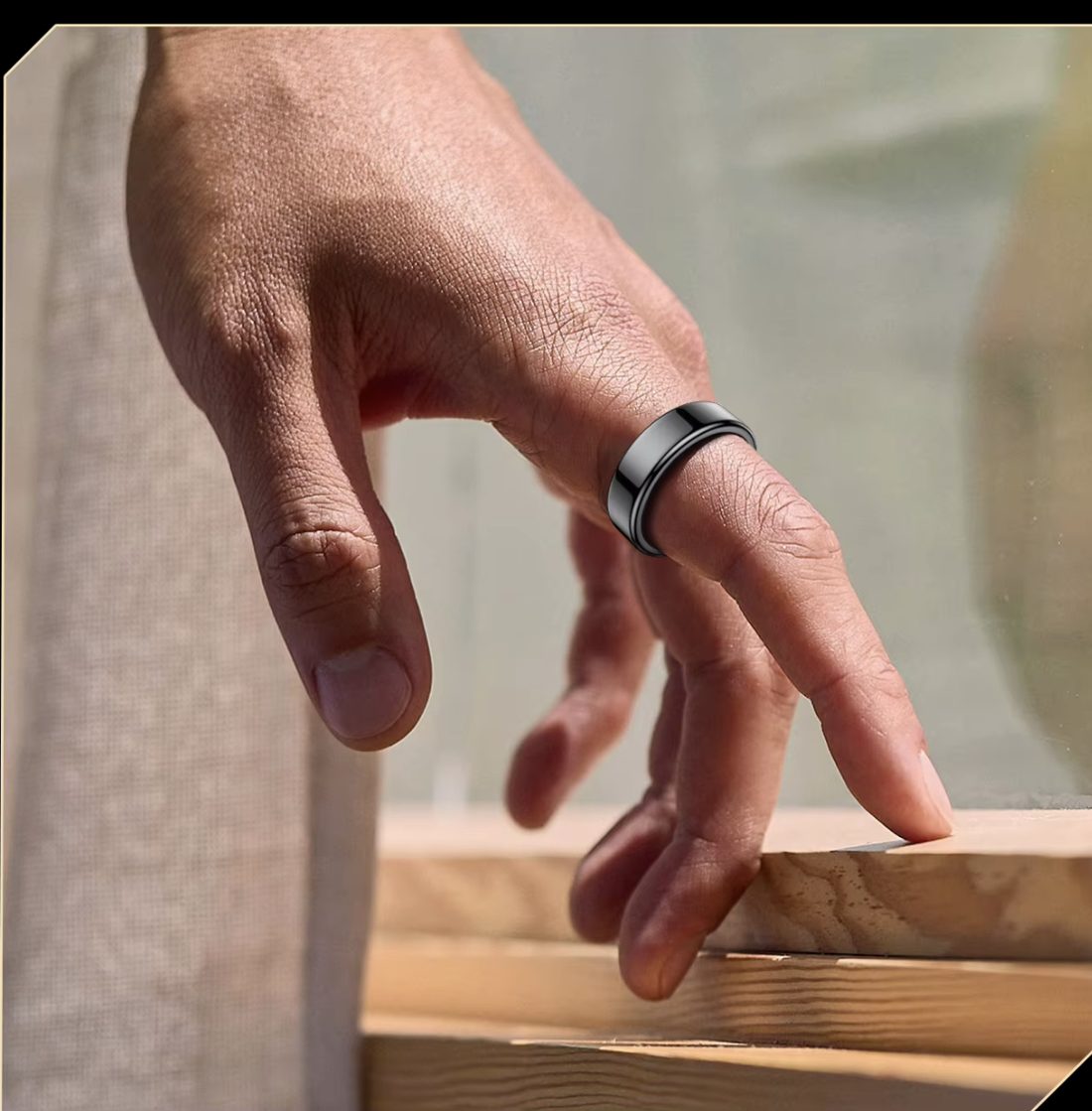 A hand wearing the Kira AI Ring in Midnight Black, resting naturally on a wooden ledge in sunlight